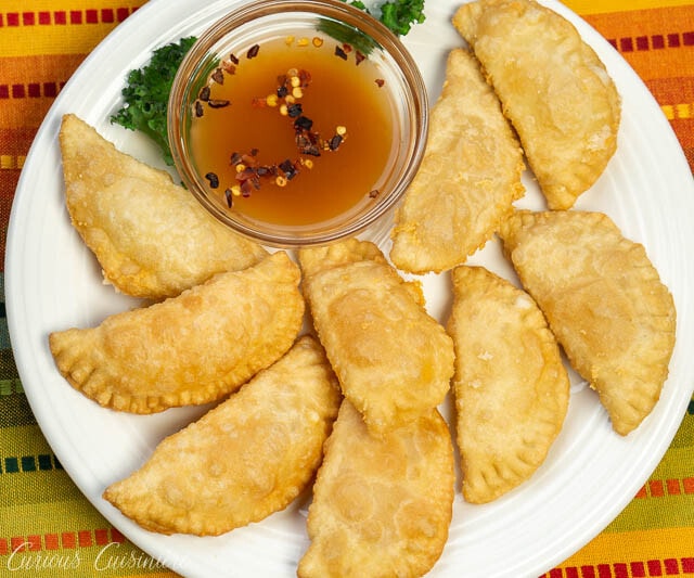 Brazilian Pastel de Queijo (Cheese Pastries) on a plate with hot sauce, overhead image