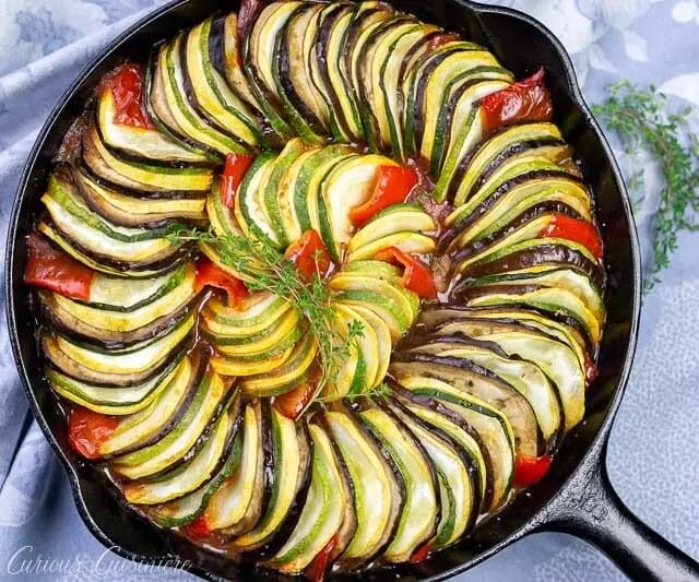 Overhead image of layered ratatouille in a cast iron skillet with eggplant, summer squash, zucchini, tomatoes, and red peppers.