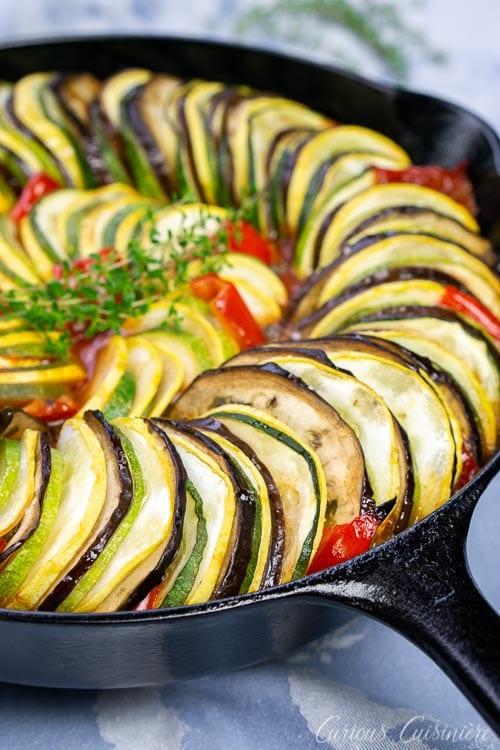 Skillet shot of baked layered ratatouillewith eggplant, summer squash, zucchini, tomatoes, and red peppers.