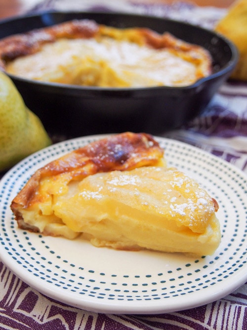 Slice of pear clafoutis with skillet in background.