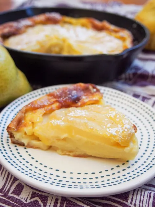 Slice of pear clafoutis with skillet in background.