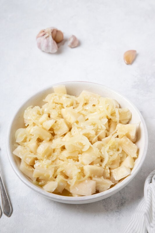 Cuban Yuca con Mojo - Cassava with garlic sauce plated next to a garlic clove