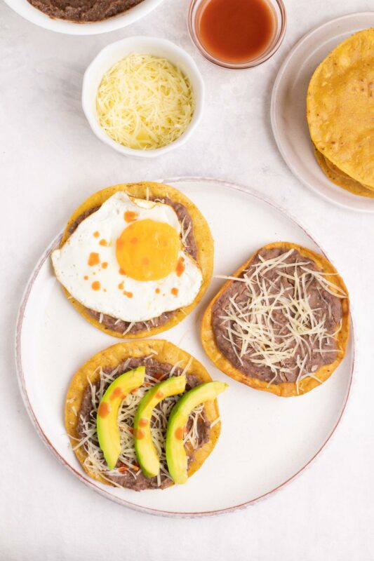 Catrachas Honduran bean and cheese tostadas with avocado and egg toppings